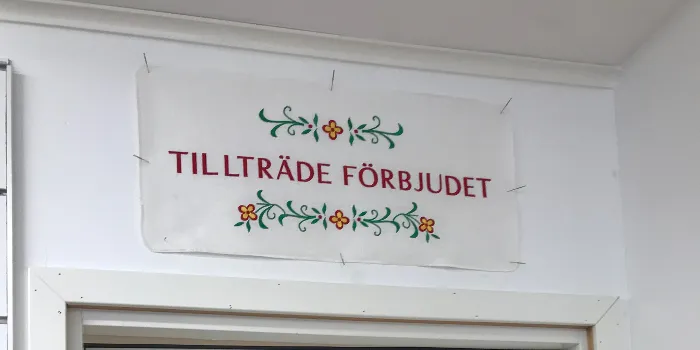 Broderad bonad monterad över dörren till vår brodyrverkstad med texten 'Tillträde Förbjudet' och blommor i kurbits stil.