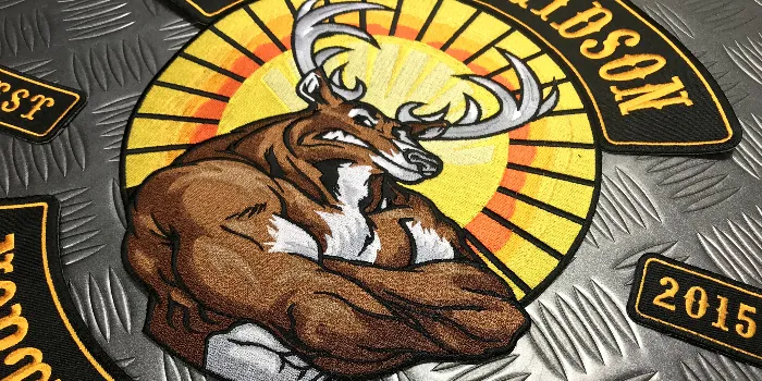 Närbild på broderat MC-märke där club-logon föreställer en muskulös ren med armarna i kors och en nedgående sol bakgrunden.