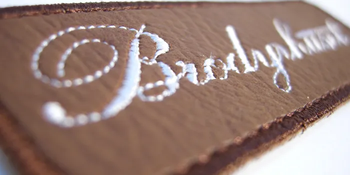 Botten i brunt läder på detta brodyrmärke skapar en fin kontrast mot den vita broderade texten.