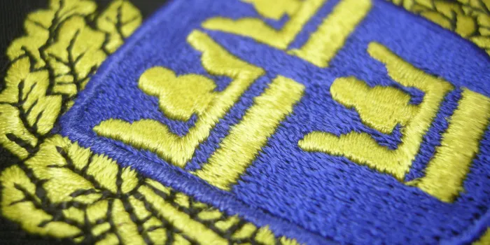 Svart brodyrmärke med 'Tre Kronor' i gult mot blå bakgrund, skapat med trådtypen 'rayon' som är standard.