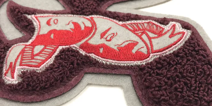Närbild på chenille patch med broderade teatermasker och utstickande bottenmaterial i vit filt som bildar en yttre kant.