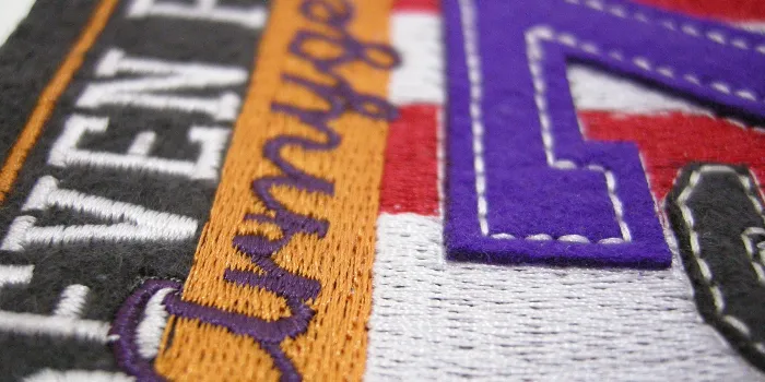 Hybridmärke med broderad bakgrund och text plus extralager med stor siffra och bokstav skapad med applikation.