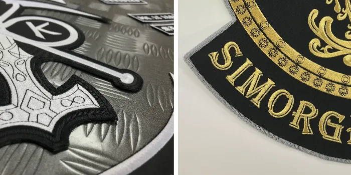 Två broderade MC-märken med olika kanter, en med broderad kan och den andra med langetterad kant.