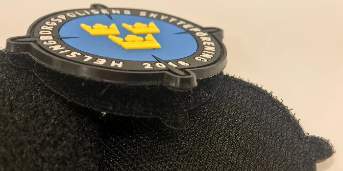 Närbild på hårkorsformat gummimärke med tre kronor och kardborrebaksida för att fästas med.
