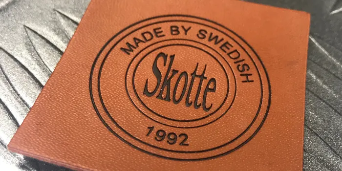 Skinnmärke med debossed(nedsänkt relief) logotyp som dessutom kombinerats med tryck.