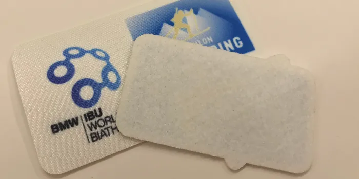 Framsidan och den helt obehandlade baksidan på ett tryckt tygmärke ämnat att sys fast.