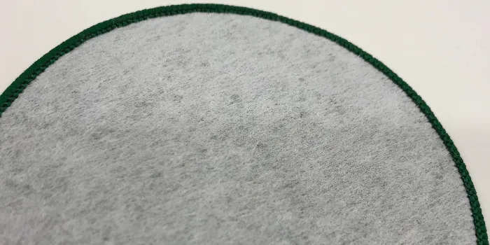 Tryckt tygmärke med baksidan förstärkt av vit non-woven vlieseline och kant mörkgrön langetterad kant.