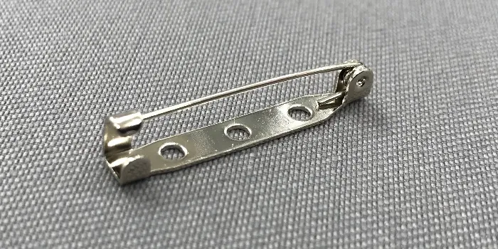 Vävt tygmärke med med praktisk broschnål fäst på baksidan.