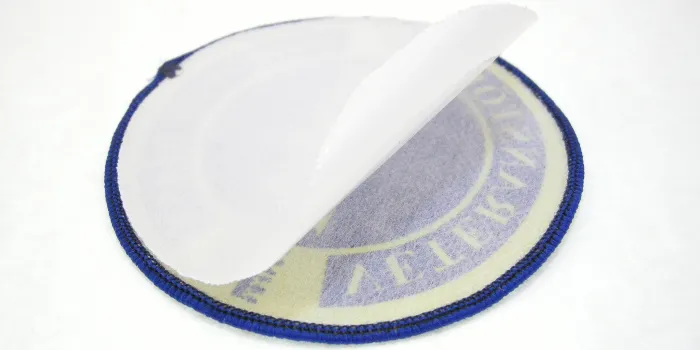 Baksidan på ett vävt tygmärke med lim som ett klistermärke och skyddspapper.