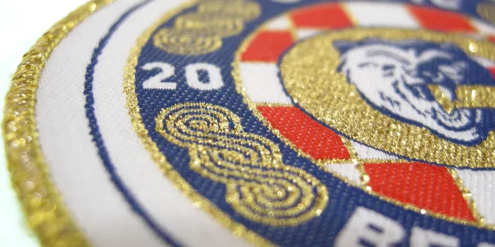 Spektakulärt exempel på vävd patch med delar vävda i guldblänkande metallisk tråd tillsammans med rött, vitt och blått.